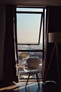 Empty chairs and table by sea against sky seen through window