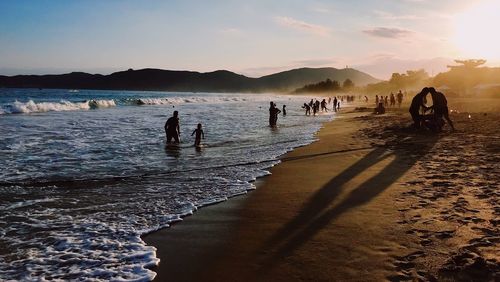 People on beach against sky during sunset