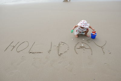 High angle view of girl crouching by text on sand at beach