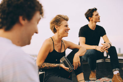 Smiling female listening music on speaker while sitting with friends on terrace at party