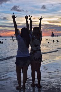 Rear view of people standing at beach during sunset