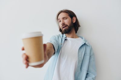 Portrait of young woman drinking coffee against white background