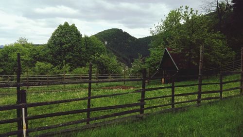 Fence on grassy field against cloudy sky