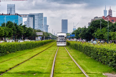 Train by railroad tracks in city against sky