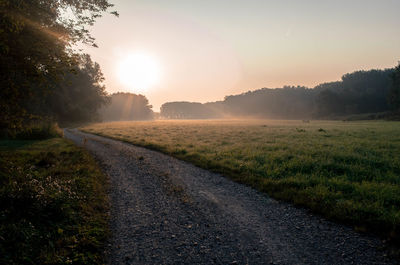 Road amidst field against clear sky during sunset