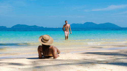 Rear view of woman standing at beach against sky