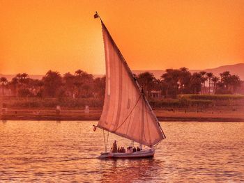 Sailboat sailing in sea at sunset