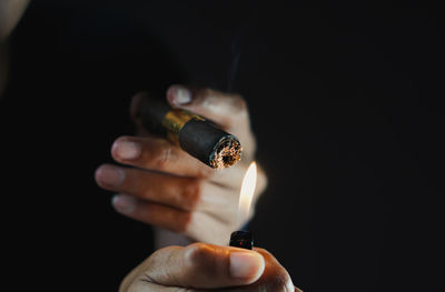 Close-up of hand holding cigarette against black background