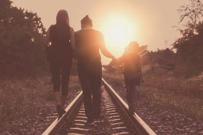 Rear view of family walking on railroad track against sky during sunset