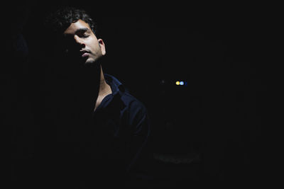 Young man with eyes closed standing against black background