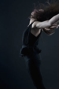 Side view of young woman standing against black background