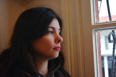 Thoughtful young woman looking through window while standing at home