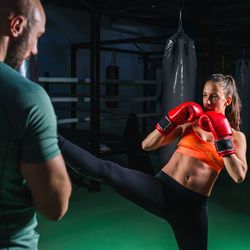 Young female boxer practicing while coach standing by punching bag