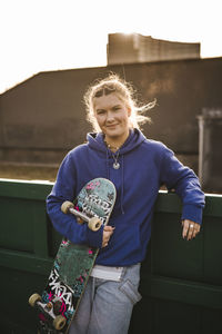 Portrait of smiling teenage girl holding skateboard