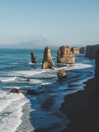 Rock formation by beach against sky