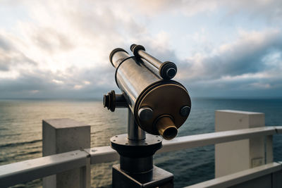 Close-up of telescope by sea against sky