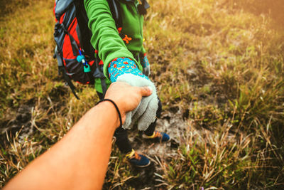 Low section of woman holding man hand on grass