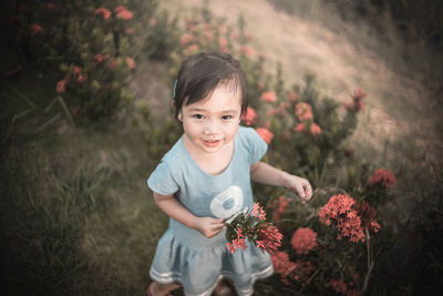 High angle portrait of smiling girl standing by ixora plant on field
