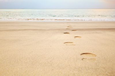 Footprints on sand at beach against sky