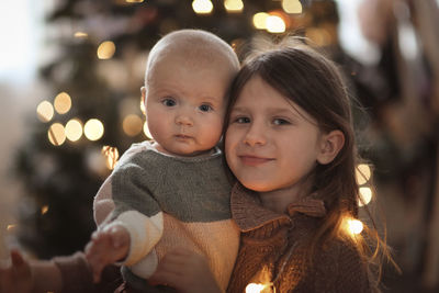 Baby and her older sister on the background of the christmas tree, the concept of christmas. 