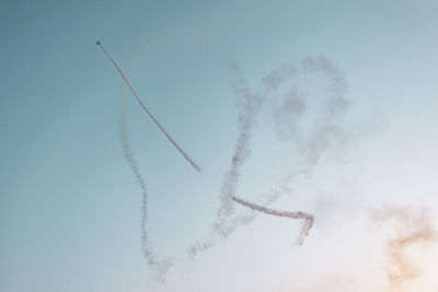 Low angle view of airplane making heart shape while flying in sky