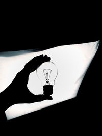 Silhouette cropped hand holding light bulb against illuminated light