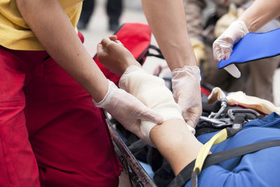 Cropped hands of people bandaging man indoors