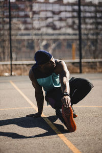 Young man stretching hand on basketball court during sunny day