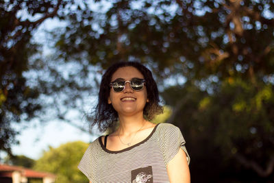 Portrait of young woman wearing sunglasses against trees