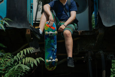Low section of man sitting with skateboard on train