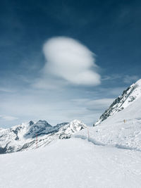 Ski trail heading into panoramic background with a conspicuous cloud above snow covered mountains