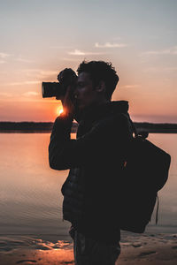 Woman photographing sea against sky during sunset