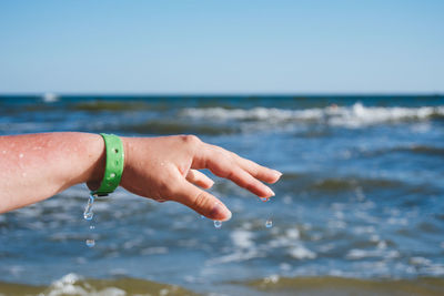 Close-up of hands over sea against blue sky