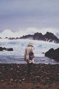 Man standing on rock by sea against sky