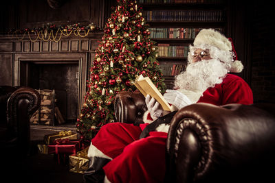 Man wearing santa claus costume reading book on sofa at home