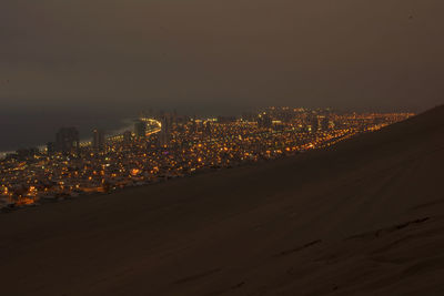 Illuminated cityscape by desert against sky at night