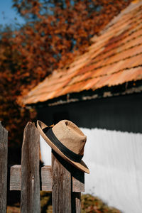 Close-up of wooden fence and hat against rustic house