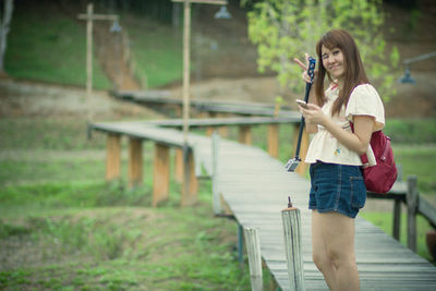 Portrait of woman gesturing while using mobile phone on footbridge