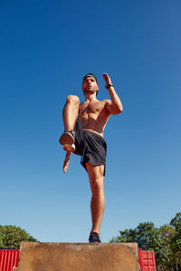 Low angle view of man exercising against clear blue sky