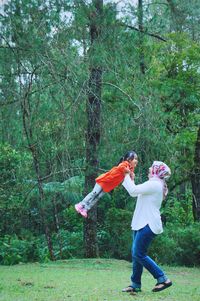 Mother carrying daughter against trees