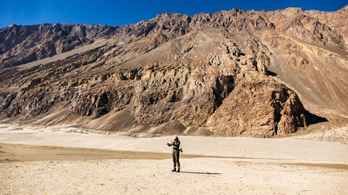 Woman photographing on sand against mountains