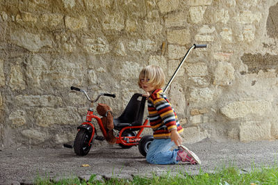 Side view of girl with bicycle against wall