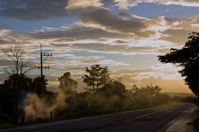 Road by trees against sky during sunset