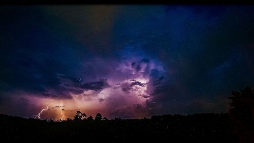 Silhouette of trees against dramatic sky at night