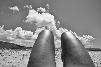 Low section of person relaxing on beach against sky