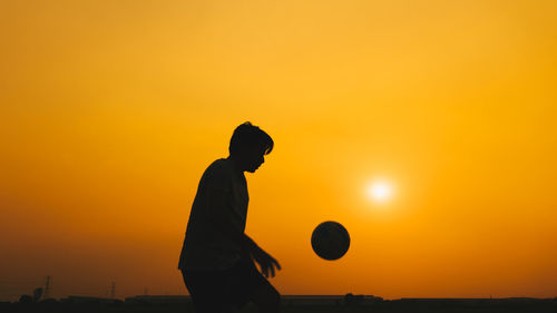 Side view of silhouette man standing against orange sky