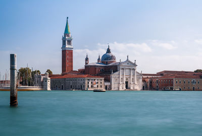 View of buildings by canal against sky in city