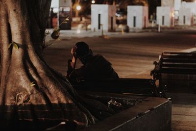 Man sitting on bench by street in city at night