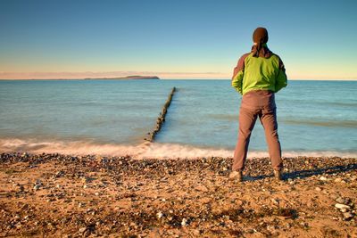 Man in green windcheater stand above bay and looki at sea far horizon. cold weather at ocean.