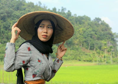 Beautiful woman in asian style conical hat looking away on field